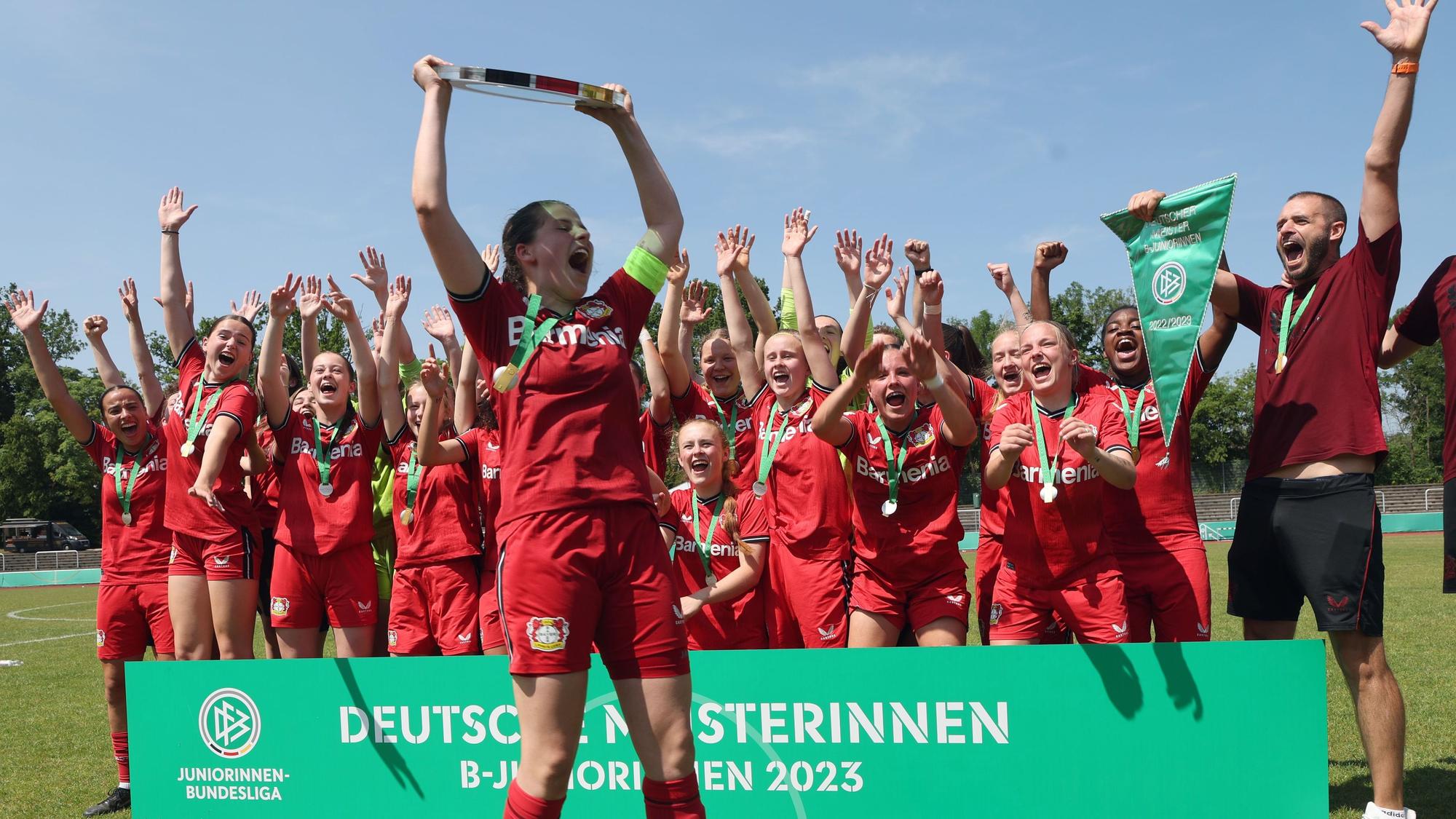 Zu sehen ist eine Mädchenmannschaft, die einen Pokal in die Höhe stemmt und feiert.