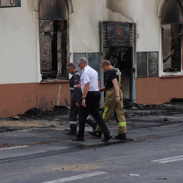 Drei Männer in Funktionskleidung gehen mit gesenkten Blicken auf das ausgebrannte Haus in Sankt Augustin zu.