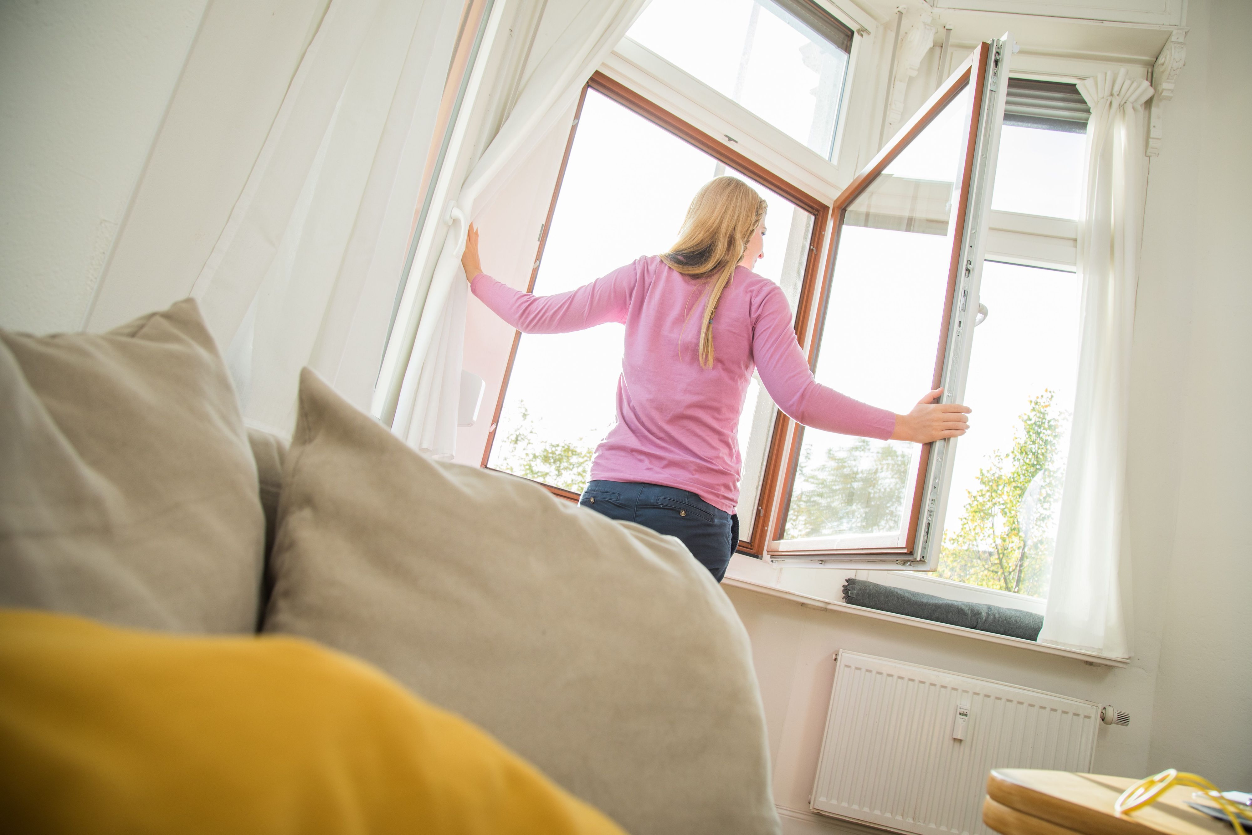 Eine Person steht an einem offenen Fenster innerhalb einer Wohnung und schaut nach draußen.
