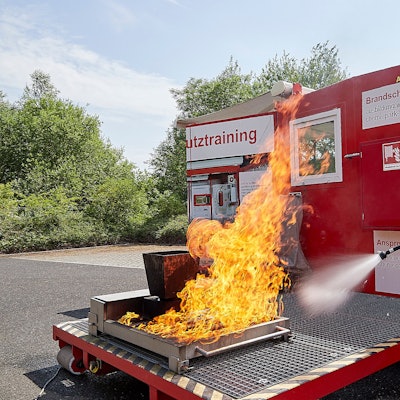 Ein Feuerwehrmann zielt mit einem Feuerlöscher auf eine Flamme.