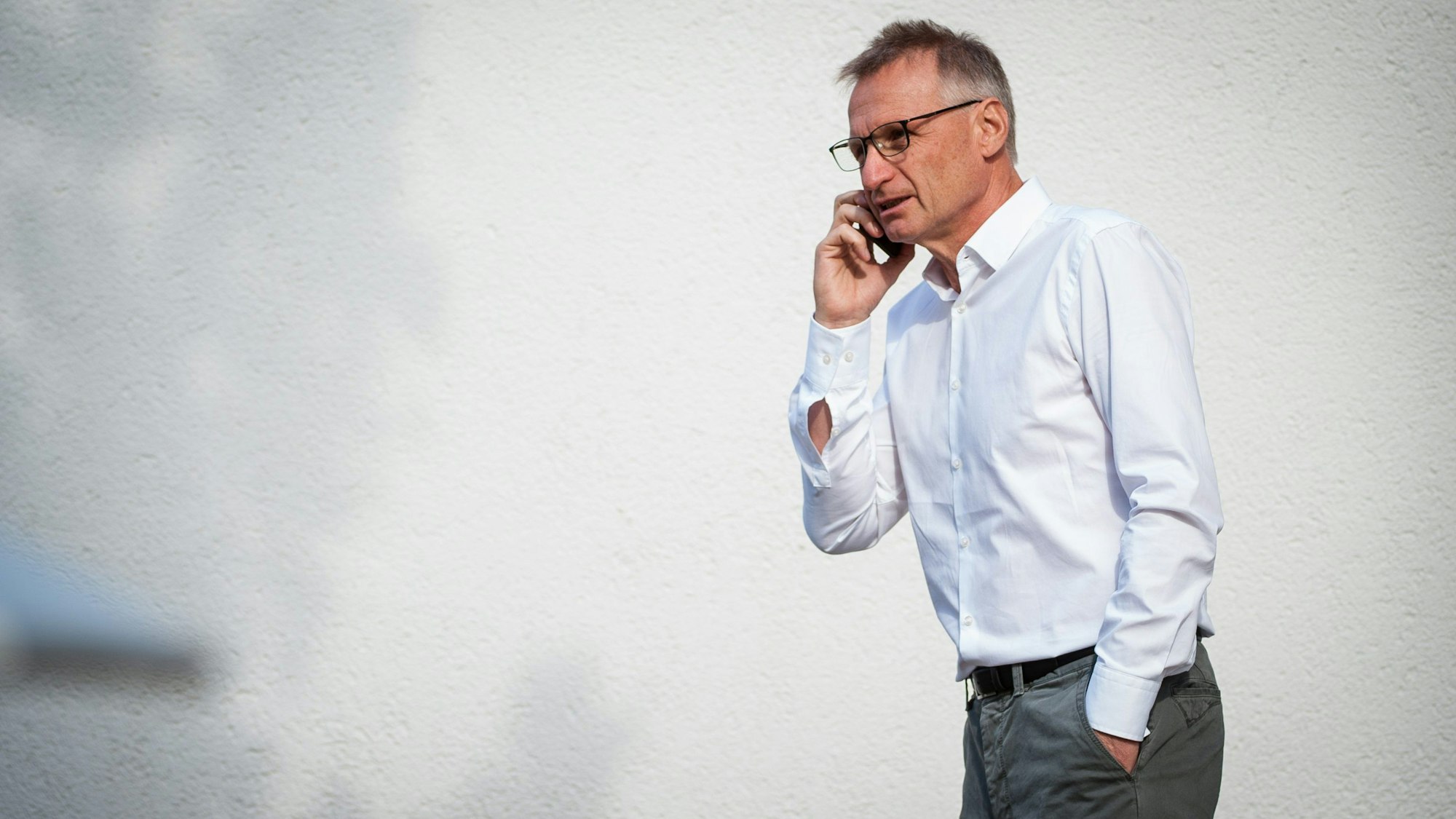 Der Fußballfunktionär Michael Reschke telefoniert mit der rechten Hand am Smartphone, hat die andere Hand in der Hosentasche.