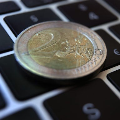 Eine Zwei -Euro-Münze liegt auf der Tastatur eines Laptops neben einem Eurozeichen.