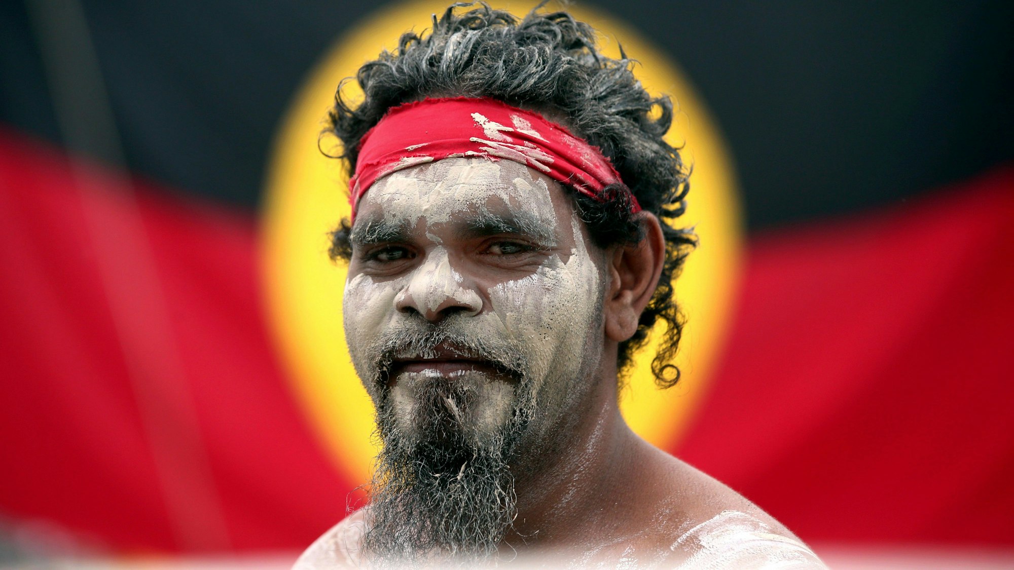 26. Januar 2018, Australien, Sydney: Stedman Sailor steht vor der Fahne der Aborigines, als er mit anderen Mitgliedern der indigenen Bevölkerung Australiens an einer Rauchzeremonie im Rahmen der Feierlichkeiten zum Australia Day teilnimmt.