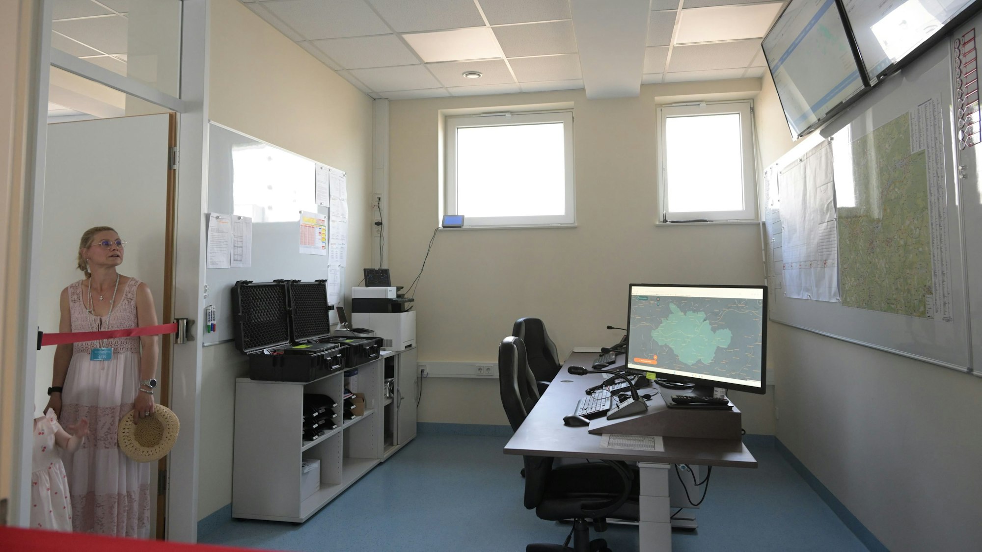 Eine Frau schaut in einen Raum mit Schreibtisch, Steuerpult und Bildschirmen.