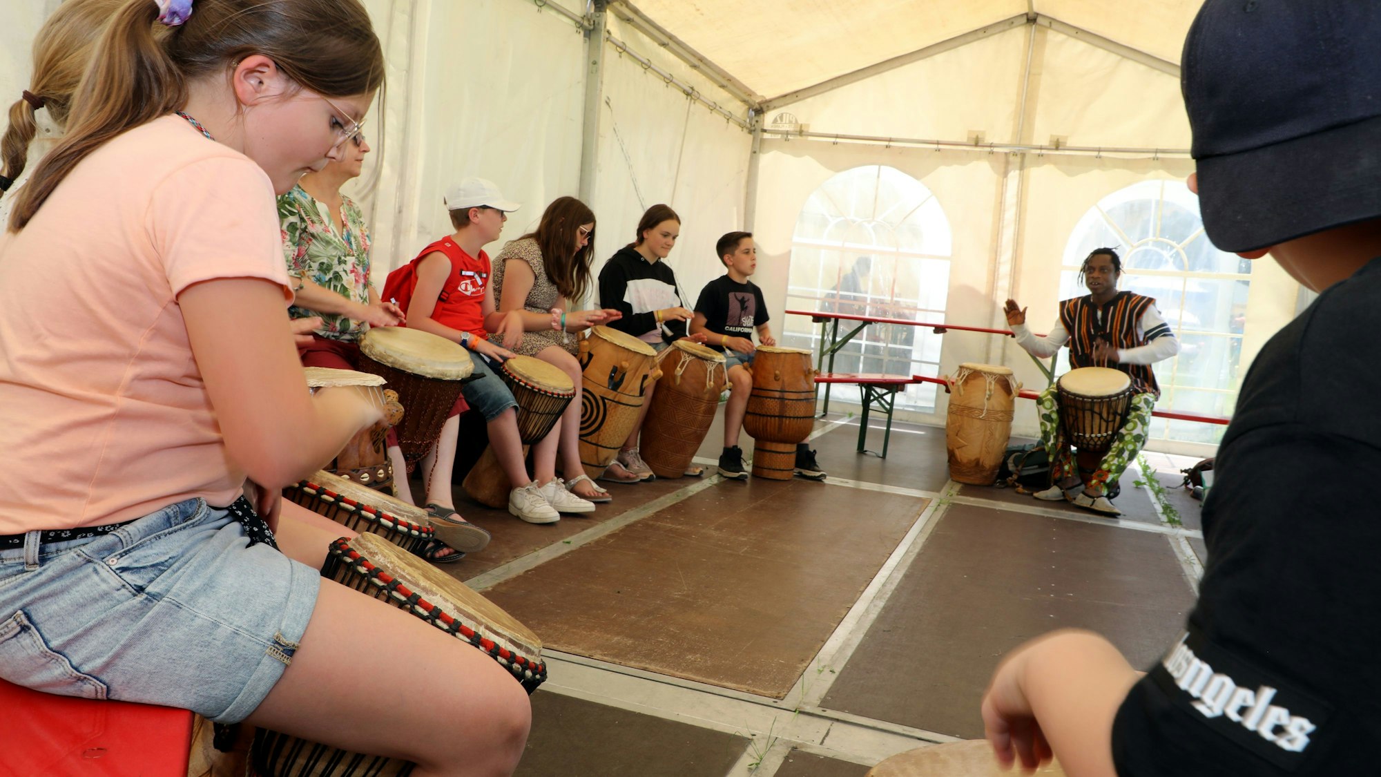 Kinder sitzen im Kreis und trommeln mit einem schwarzen Trommellehrer.