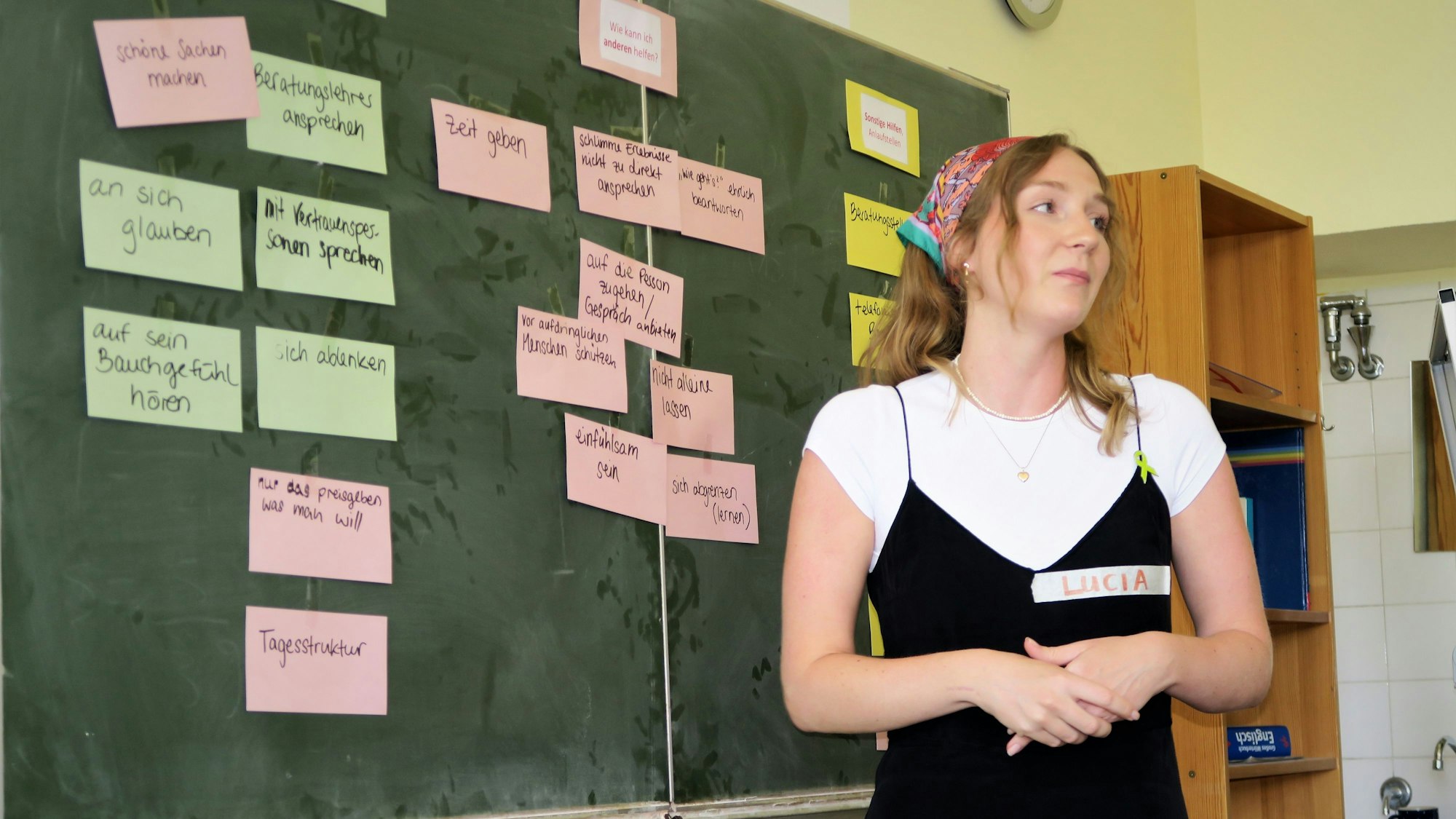 Eine junge Frau mit blonden Haaren steht vor einer Tafel.