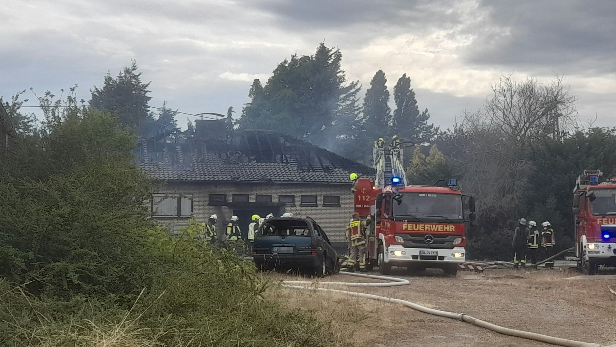 Feuerwehrwagen stehen neben einem Haus mit verbranntem Dachstuhl.