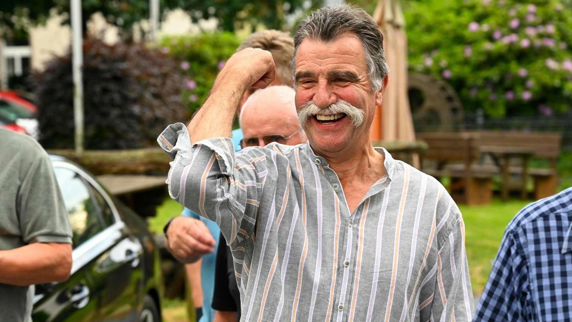 Ex-Handball-Bundestrainer Heiner Brand lacht, umgeben von mehreren Männern.