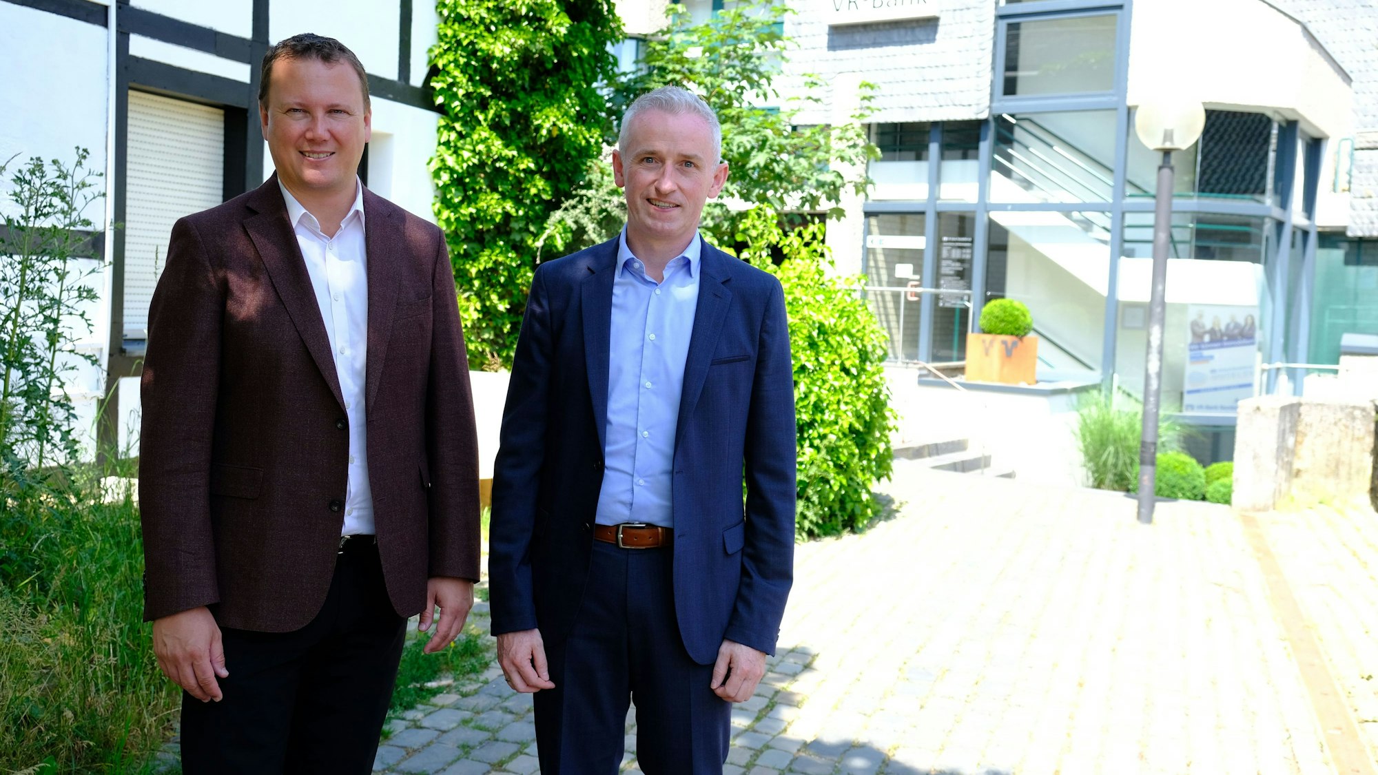 Zwei Männer im Sakko vor dem Gebäude der VR-Bank Nordeifel in Blankenheim.