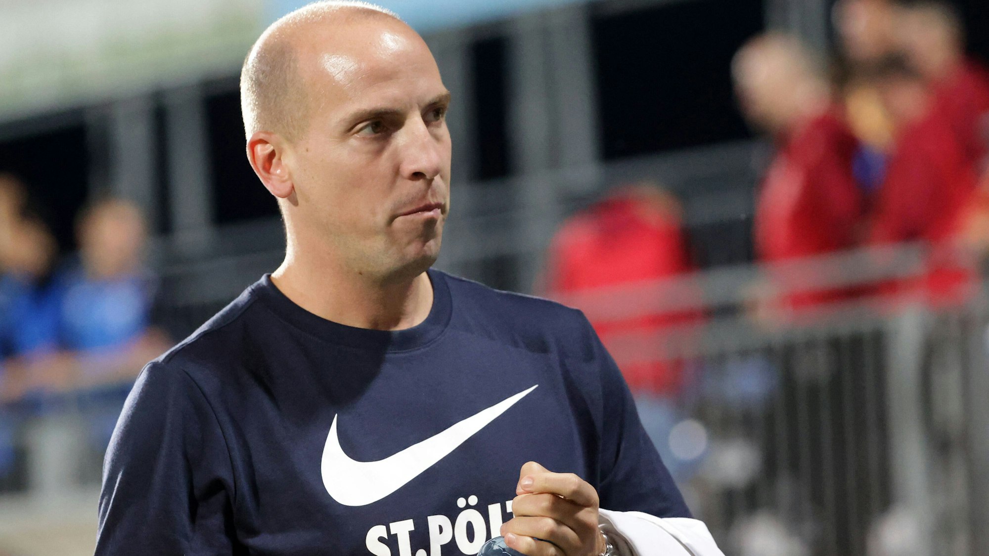 Jan Schlaudraff hat eine Wasserflasche in der Hand und schaut in die Ferne. Er befindet sich in einem Fußballstadion samt Publikum.