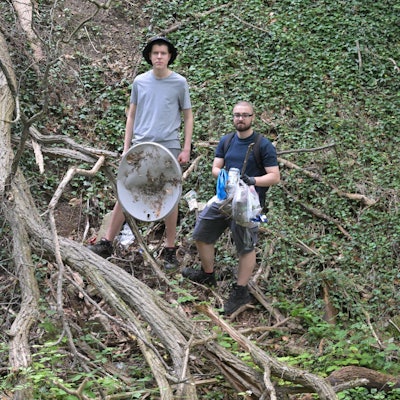 Die Jungs stehen im Wald und halten Müll in ihren Händen.