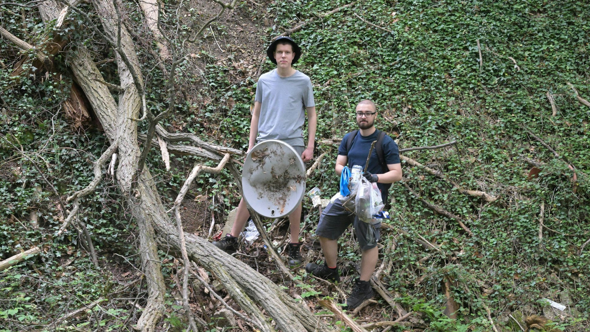 Die Jungs stehen im Wald und halten Müll in ihren Händen.