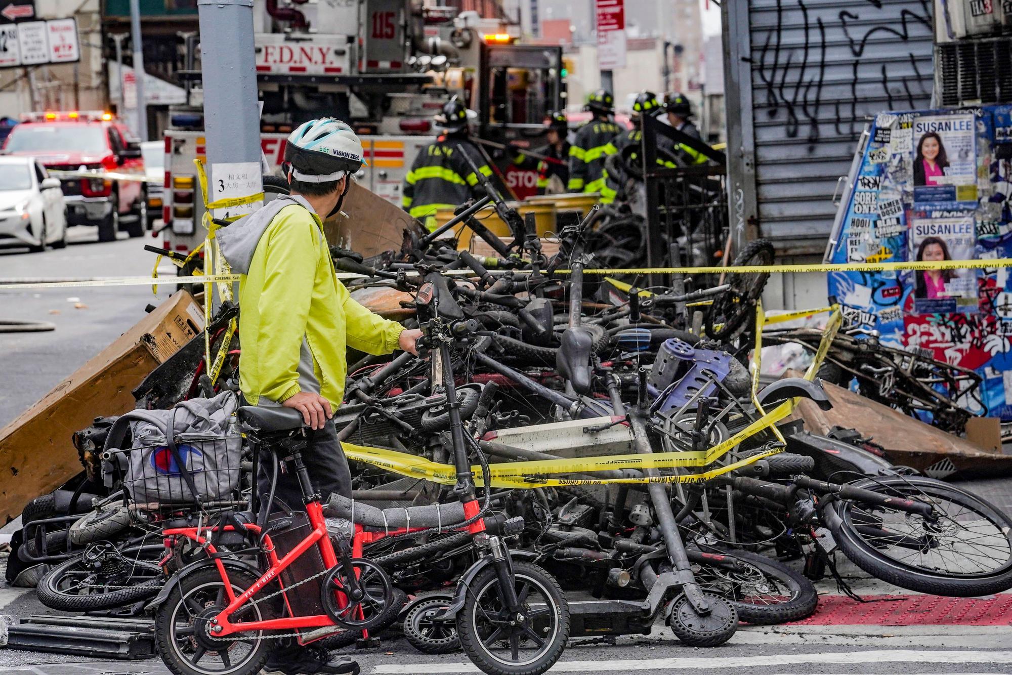USA, New York: Ein Radfahrer hält an, um einen Stapel von E-Bikes nach einem Brand in Chinatown zu betrachten, der nach Angaben der Behörden in einem E-Bike-Laden ausgebrochen ist und sich auf Wohnungen in den oberen Stockwerken ausgebreitet hat.