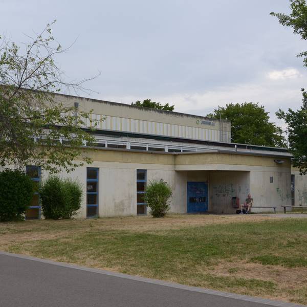 Das Bild zeigt die von Bäumen und Sträuchern umgebene Sporthalle.
