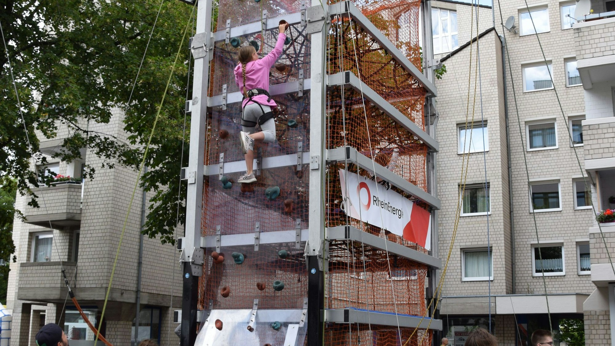 Ein Mädchen ist an Seilen gesichert und besteigt einen Kletterturm.