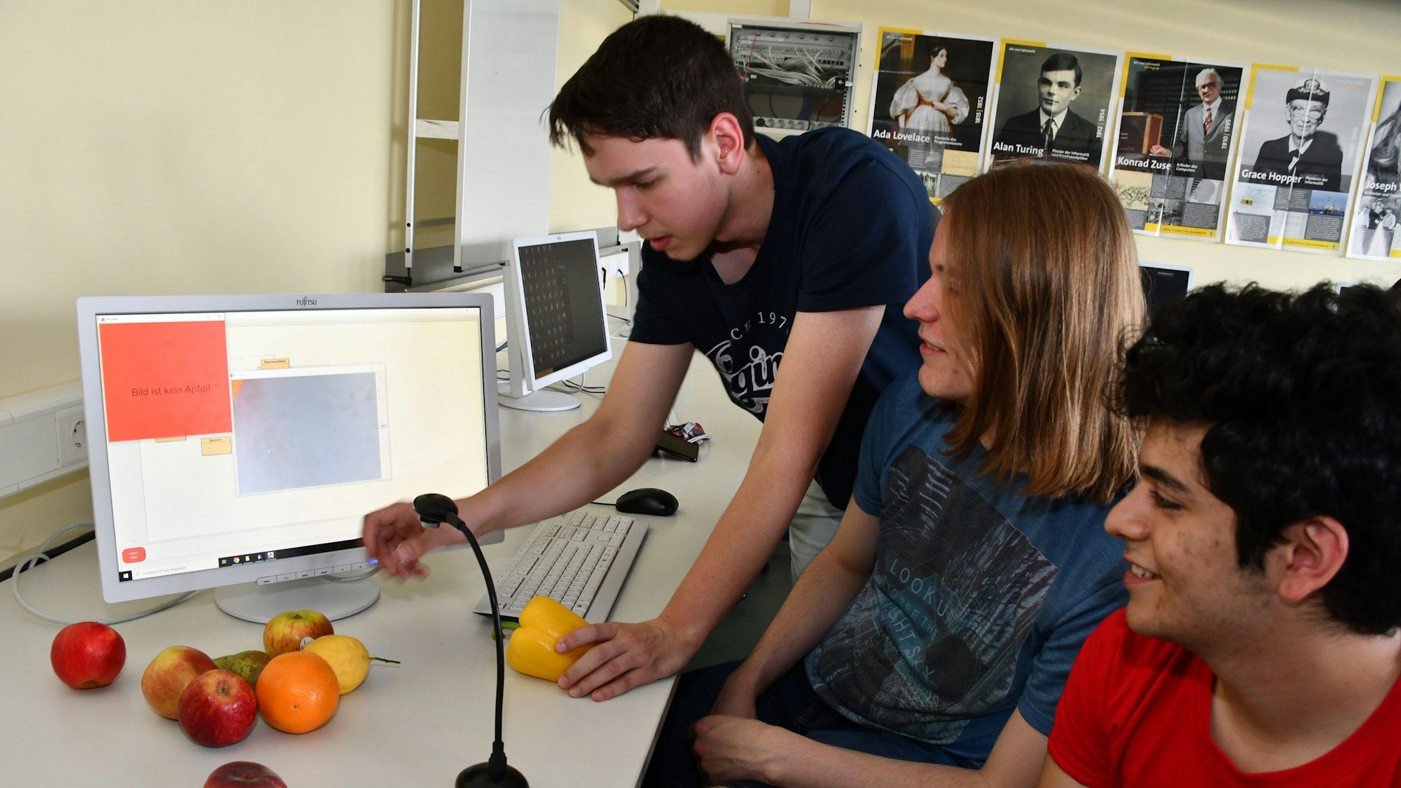 Das Foto zeigt drei Schüler und Obst vor einem Computer.