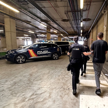 Ein Mann wird von der spanischen Polizei verhaftet abgeführt. Die auf dem Foto sichtbaren Menschen haben der Kamera den Rücken zugedreht. Im Hintergrund befinden sich Polizeiwagen.