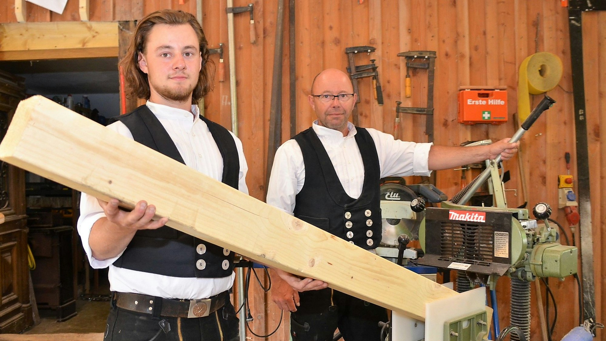 Zwei Männer halten gemeinsam einen großen, hellen Holzbank in der Hand.