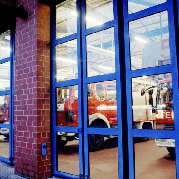 Auf dem Foto sind hinter den geschlossenen Glastüren der Feuerwehrwache Erftstadt die Rettungswagen zu sehen.