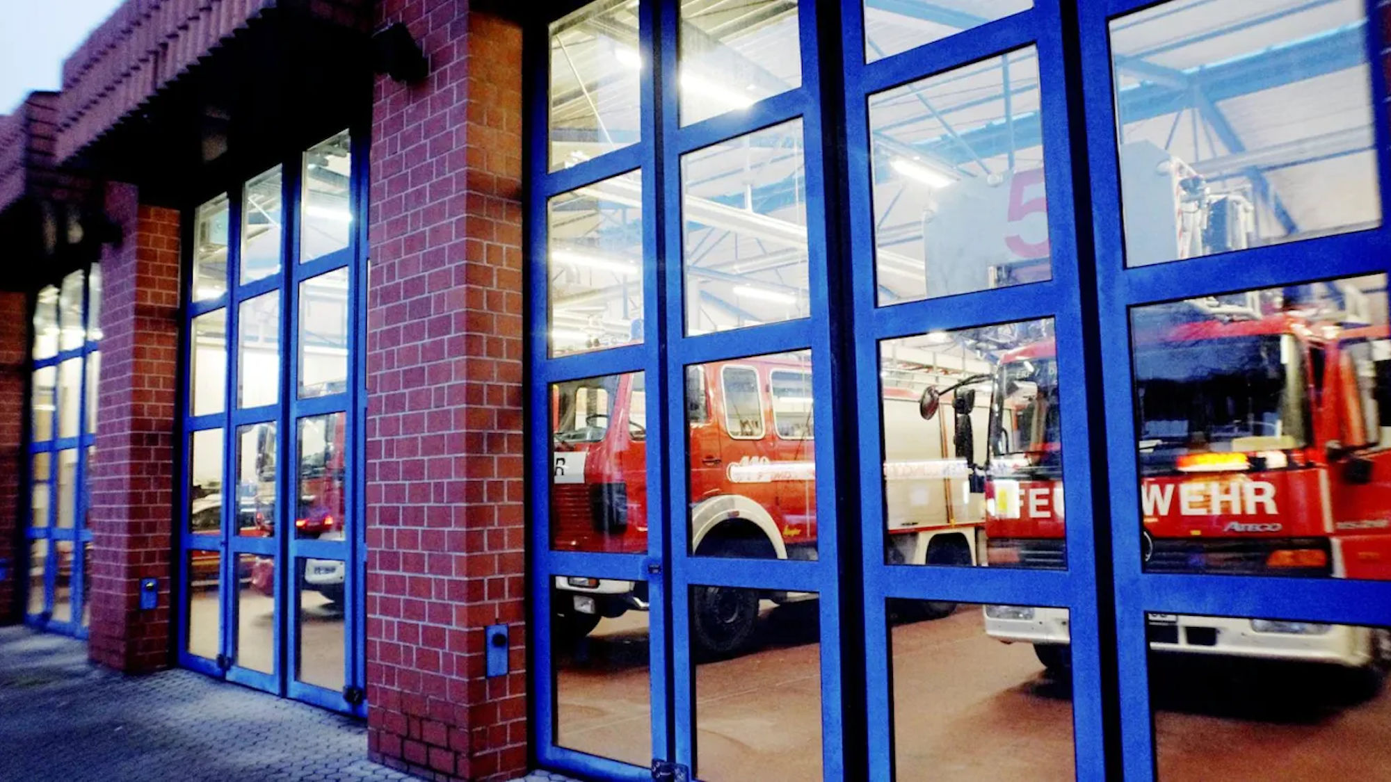 Auf dem Foto sind hinter den geschlossenen Glastüren der Feuerwehrwache Erftstadt die Rettungswagen zu sehen.