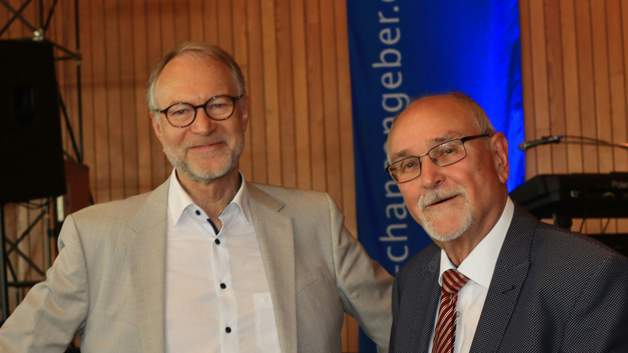 Zwei Männer stehen vor einer Bühne, einer hält Zettel in den Händen.