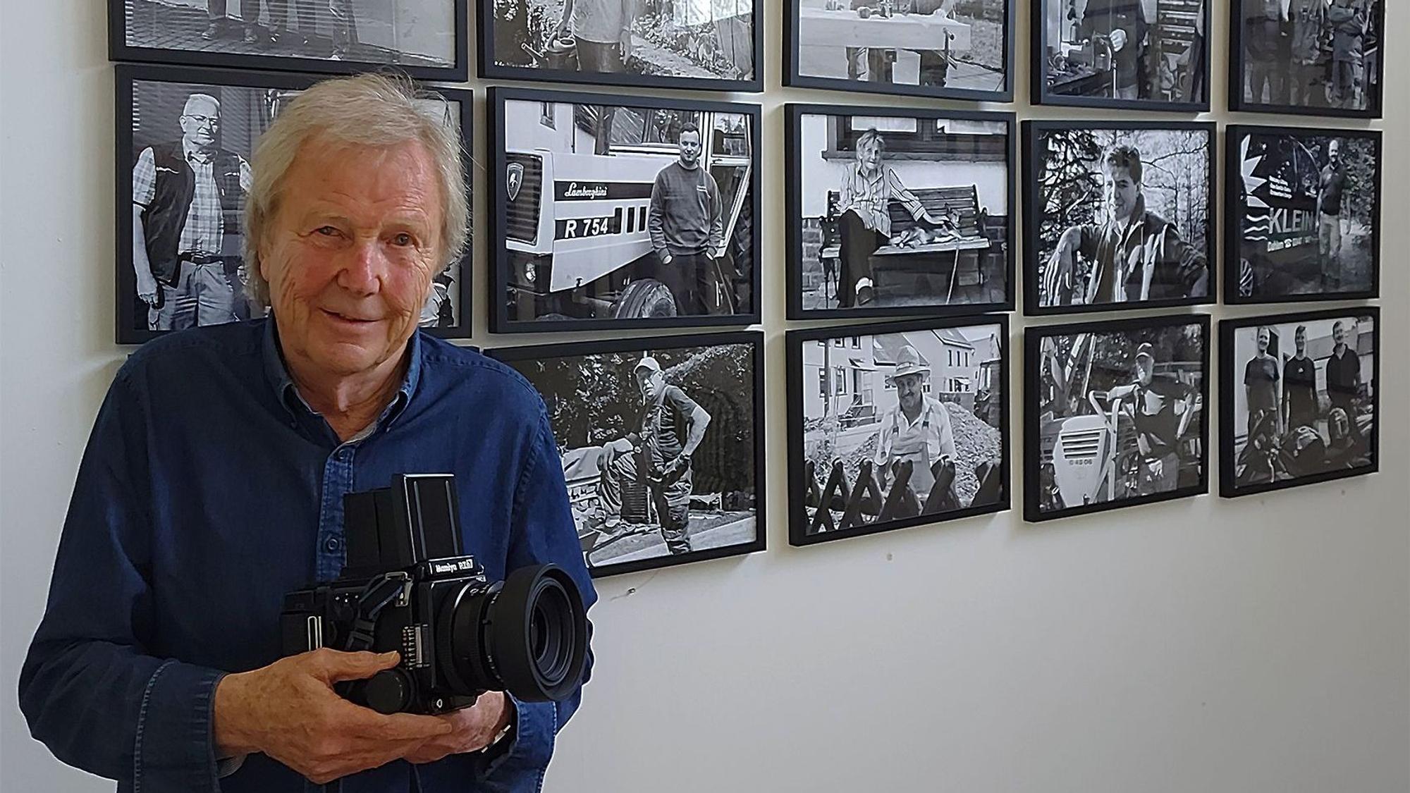 Der Fotograf Dietrich Schubert steht mit seiner Kamara vor einigen seiner Fotos.
