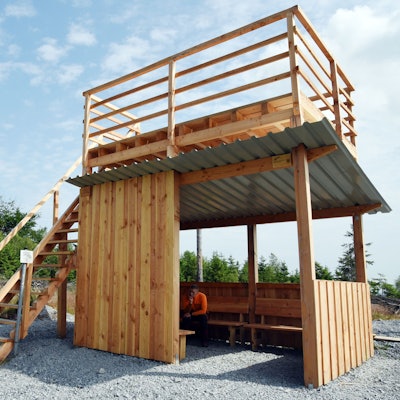 Das Bild zeigt eine Holzhütte, deren Flachdach über eine Treppe bestiegen werden kann.