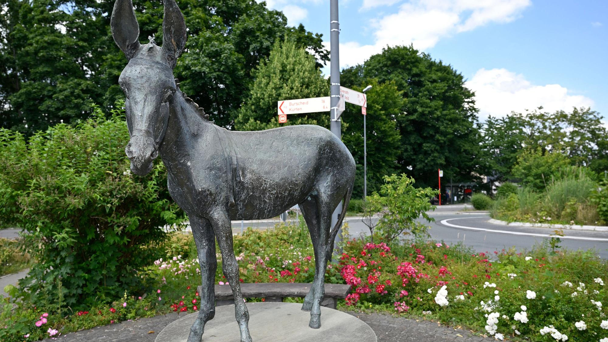 Die Skulptur des Bechener Esels steht vor Blumen.