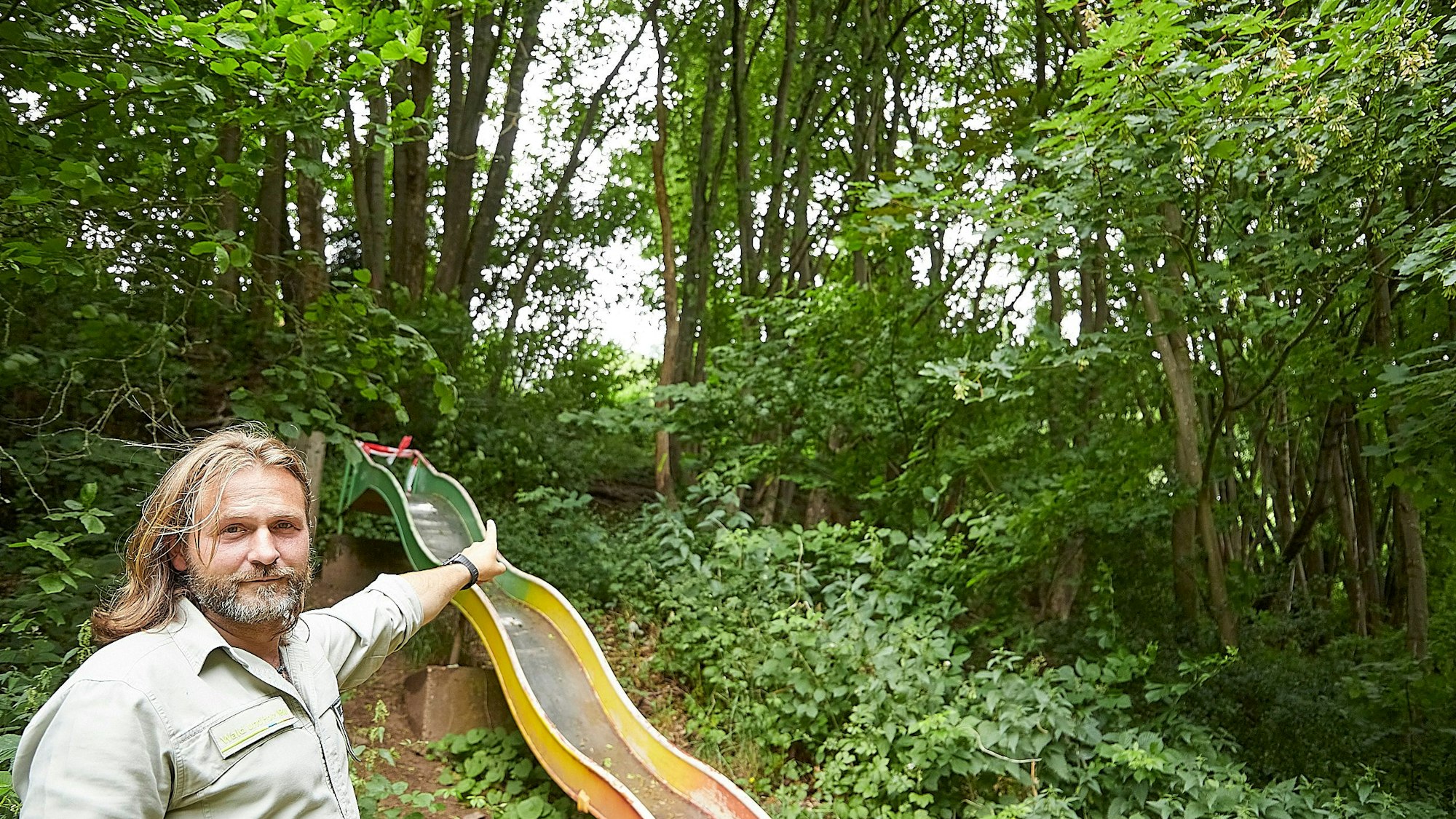 Förster Markus Wunsch zeigt auf eine Rutsche und die Bäume dahinter.