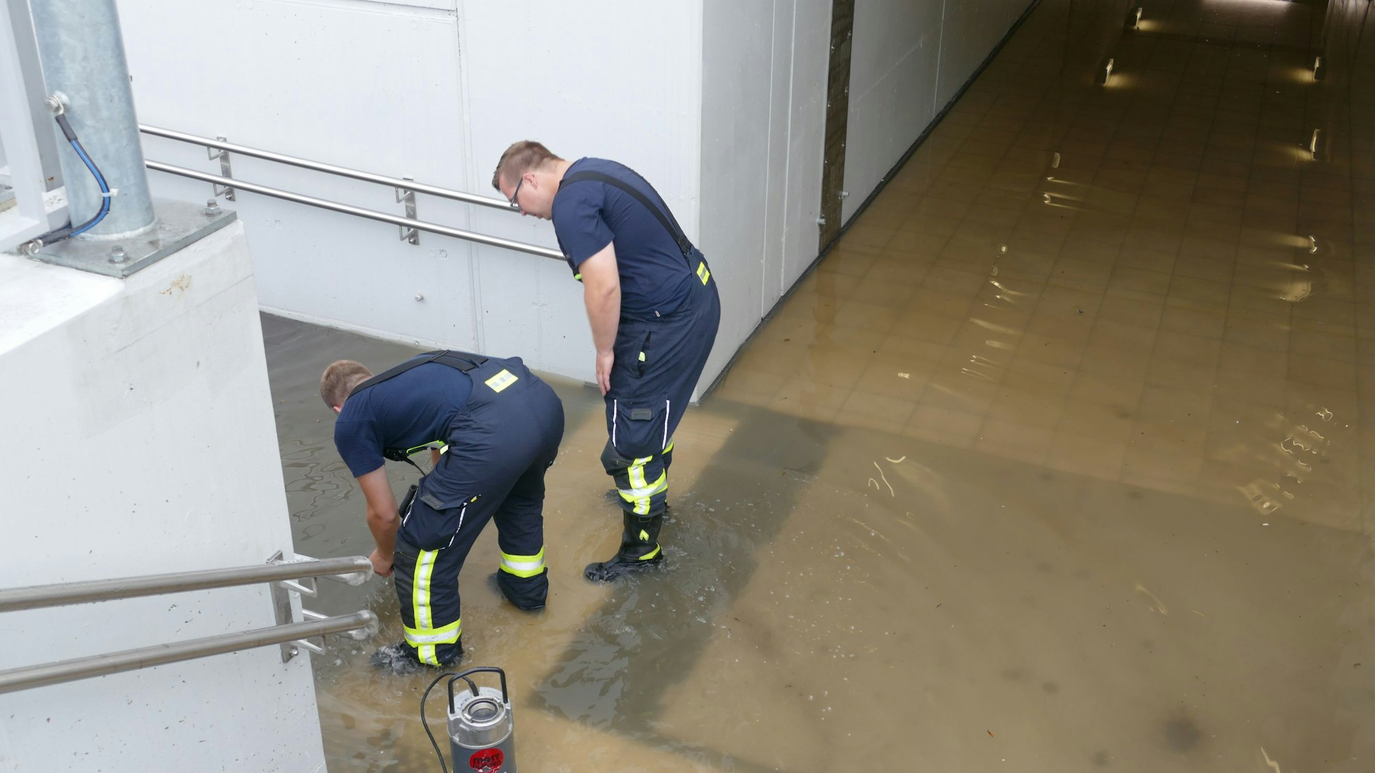Zwei Feuerwehrleute stehen in der vollgelaufenen Unterführung des Bahnhofs in Friedrich-Wilhelms-Hütte.