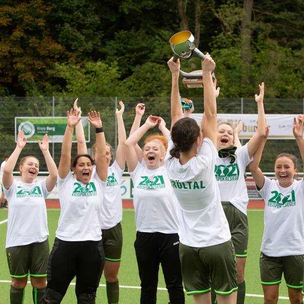 Jubelnde Fußballerinnen recken einen Pokal in die Höhe.