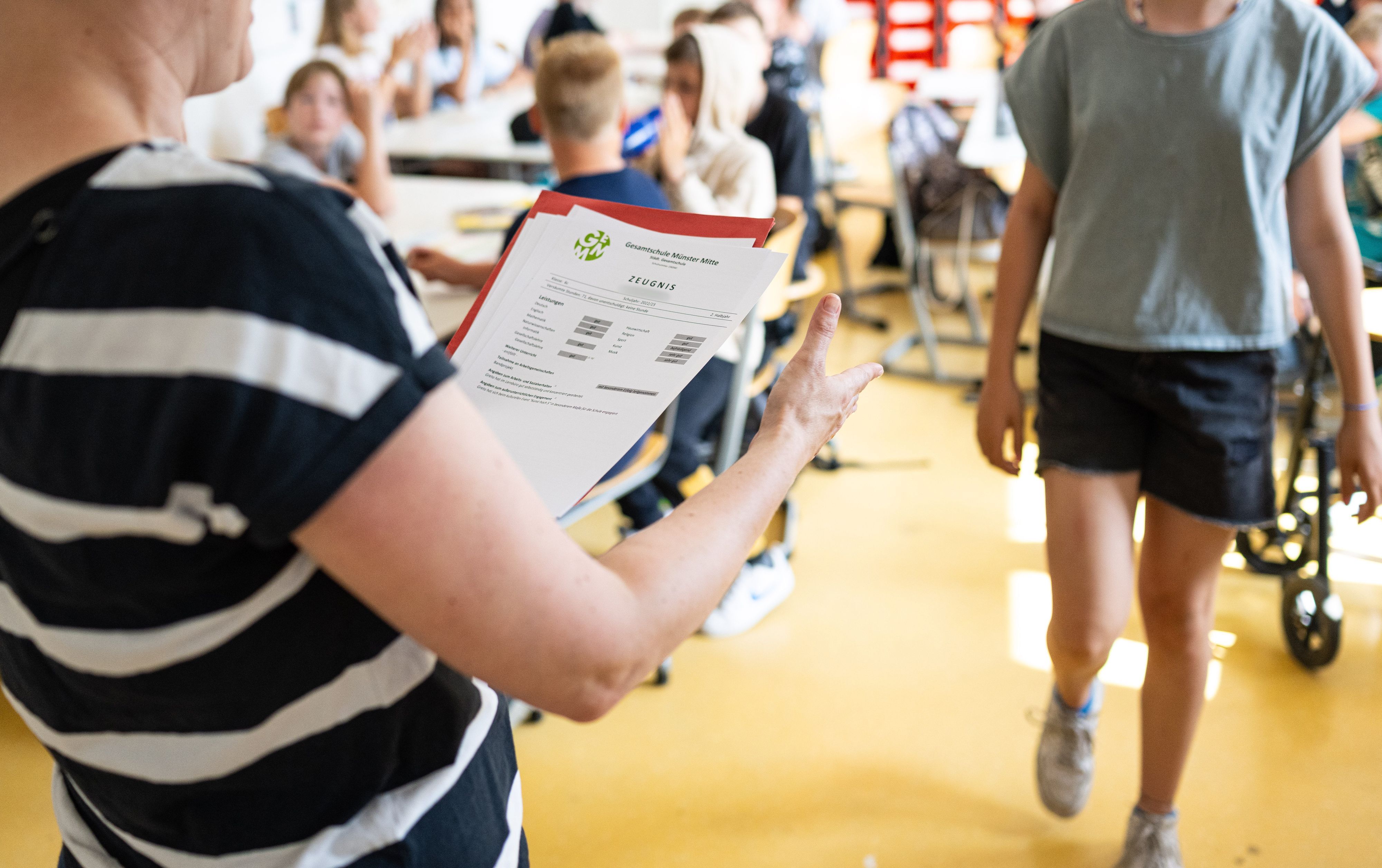 An einer Schule verteilt eine Klassenlehrerin die Zeugnisse an die Schüler.