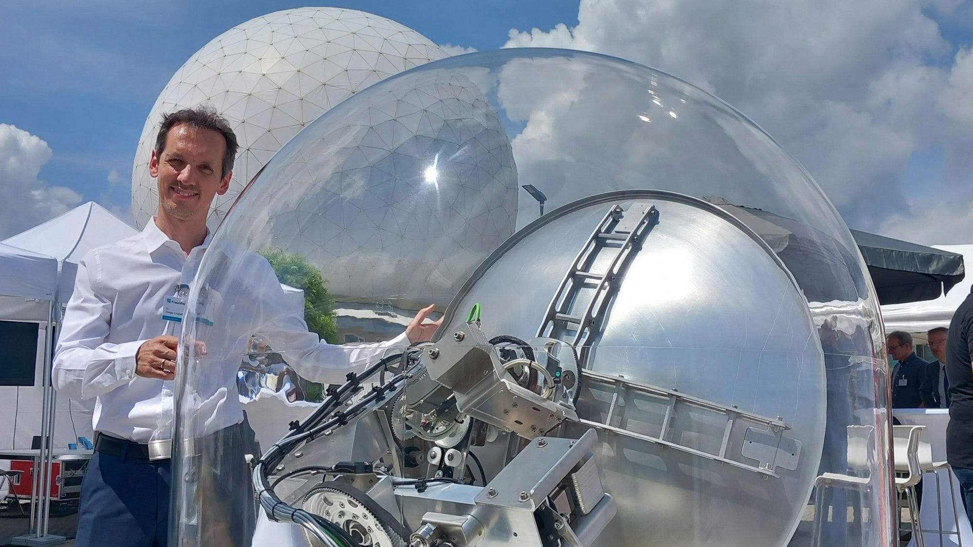 Diego Cristallini zeigt das Satelliten basierte Passivradar beim Wachtberg-Forum von Fraunhofer. Im Hintergrund das Radom in Wachtberg-Werthhoven.