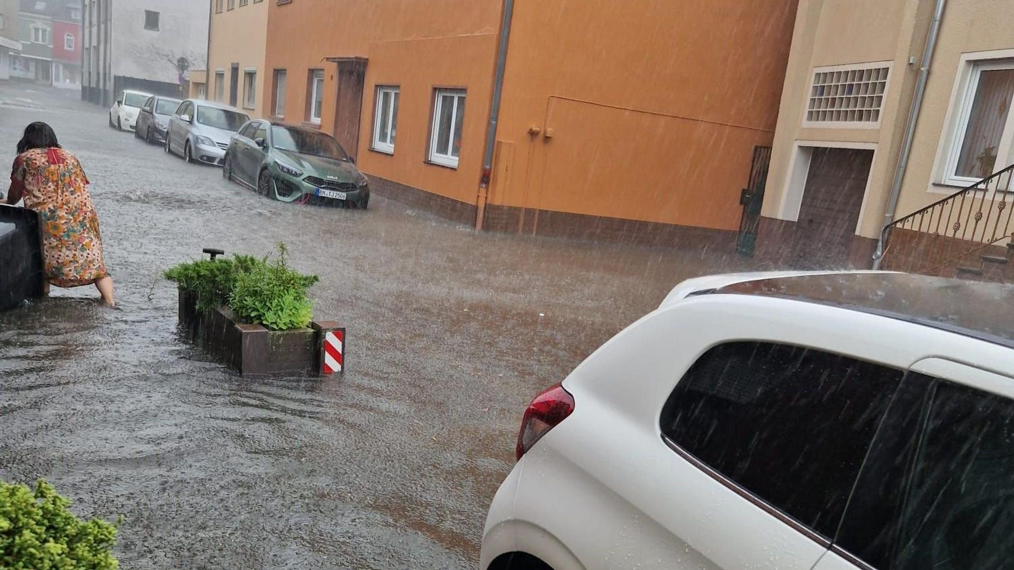Auf dem Foto ist eine Frau zu sehen, die in Bedburg versucht, eine Mülltonne zu sichern, die von den Wassermassen mitgezogen wurde.
