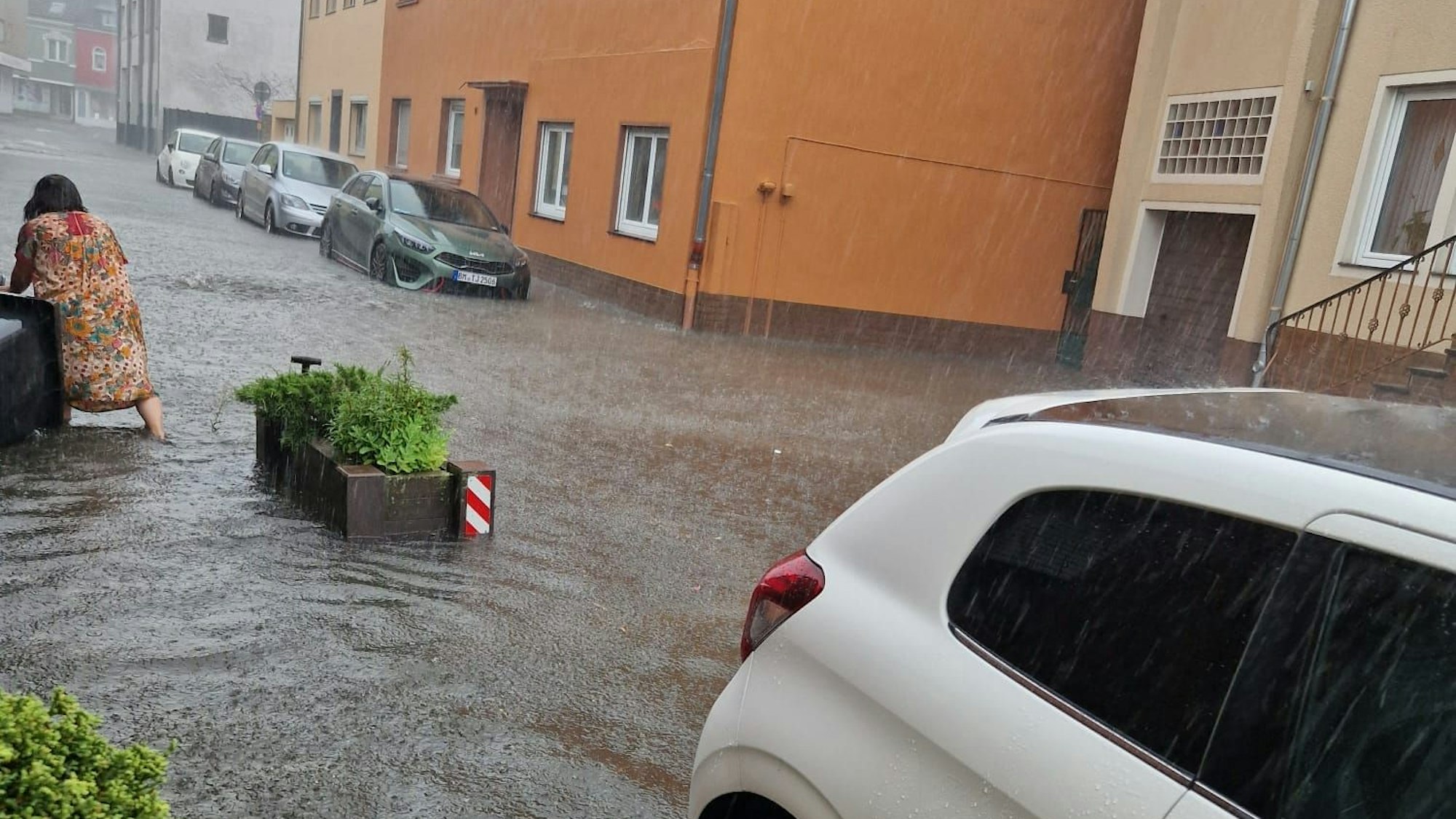 Auf dem Foto ist eine Frau zu sehen, die in Bedburg versucht, eine Mülltonne zu sichern, die von den Wassermassen mitgezogen wurde.