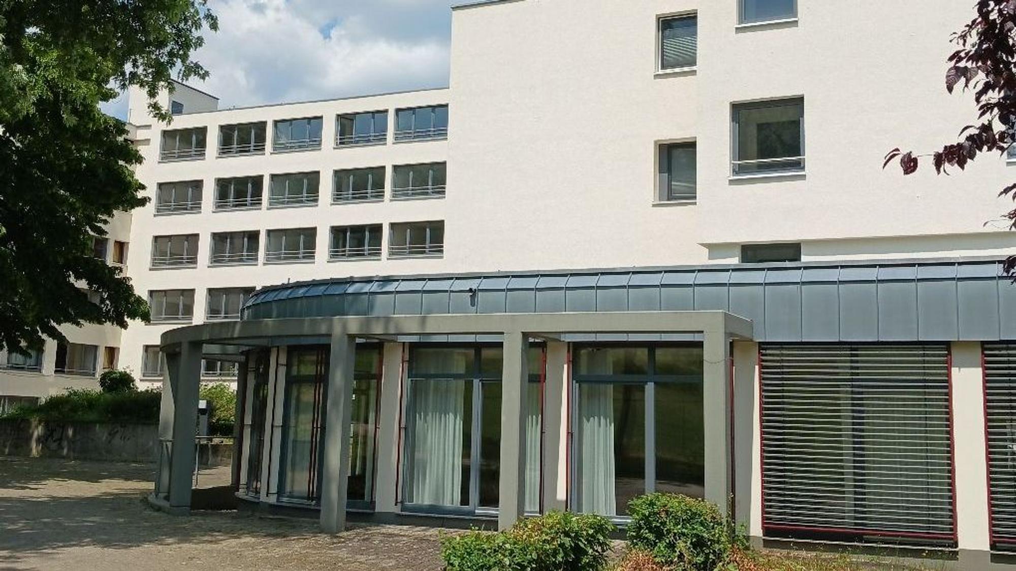 Ein modernes Wohngebäude mit fünf Etagen; im Vordergrund steht ein Anbau mit großen Fenstern.