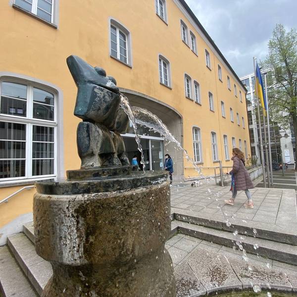 Das Bild zeigt das Brühler Rathaus, vor dem ein Brunnen sprudelt.