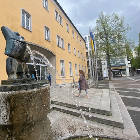 Das Bild zeigt das Brühler Rathaus, vor dem ein Brunnen sprudelt.