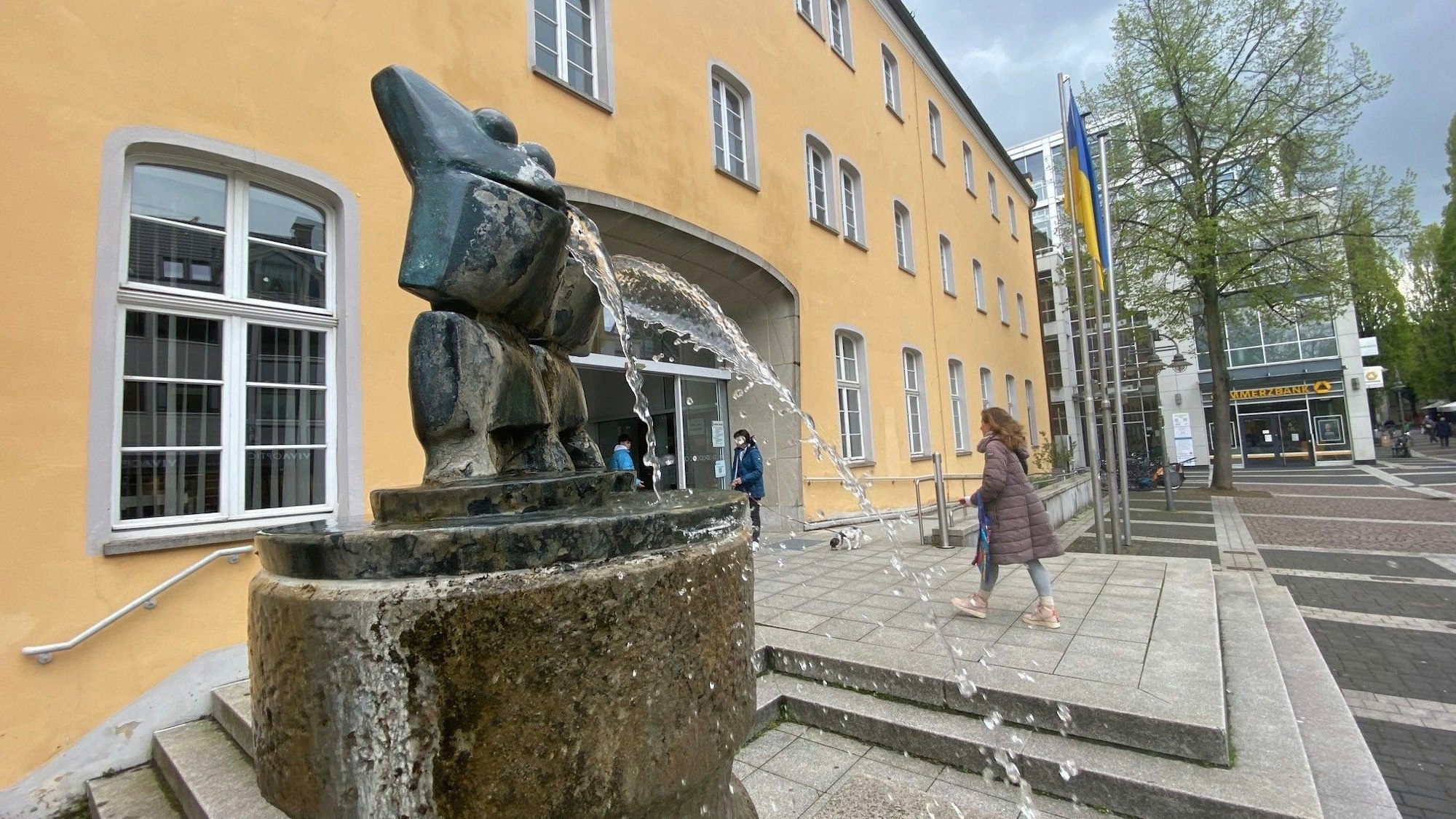 Das Bild zeigt das Brühler Rathaus, vor dem ein Brunnen sprudelt.