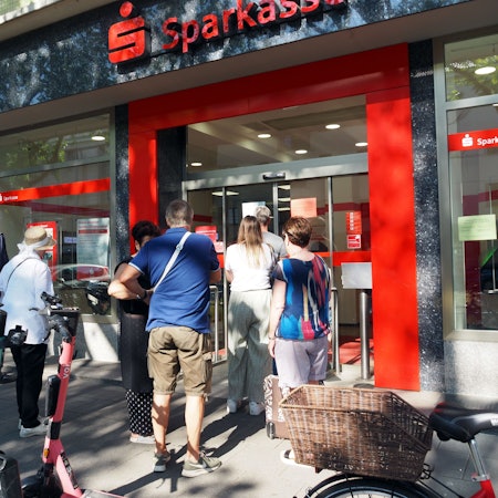 Viele Menschen stehen vor der Sparkasse.