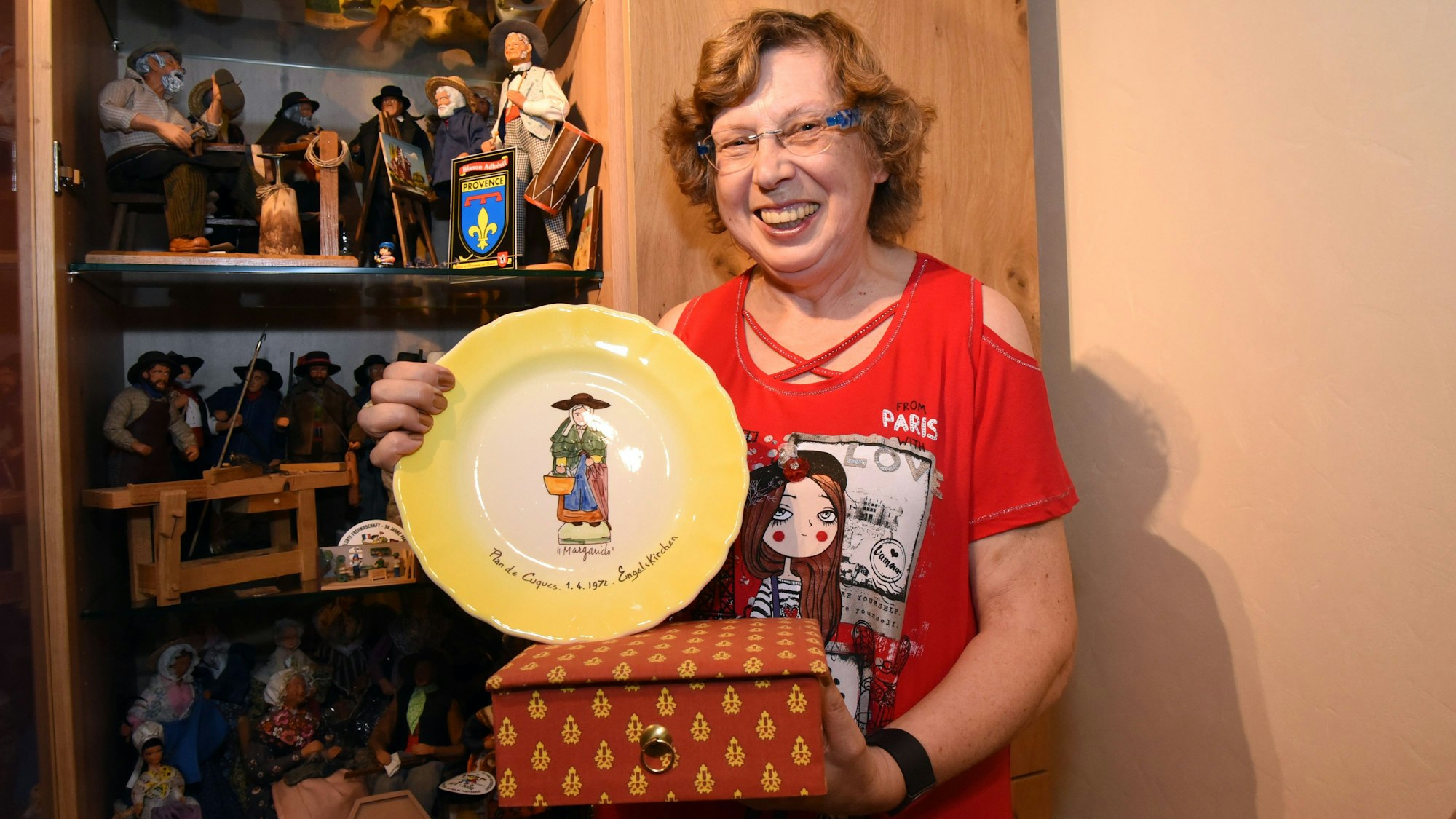 Eine Frau hält eine bunte Stoffkiste und einen Porzellanteller in einer Hand.