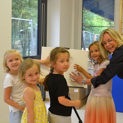 Kindergartenkinder und Bürgermeisterin drücken ihre Hände auf eine Leinwand im Kindergarten.