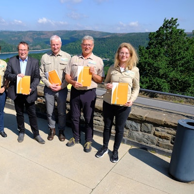 Mehrere Personen in Outdoorkleidung und ein Mann im Anzug präsentieren den Jahresbericht des Nationalparks Eifel.