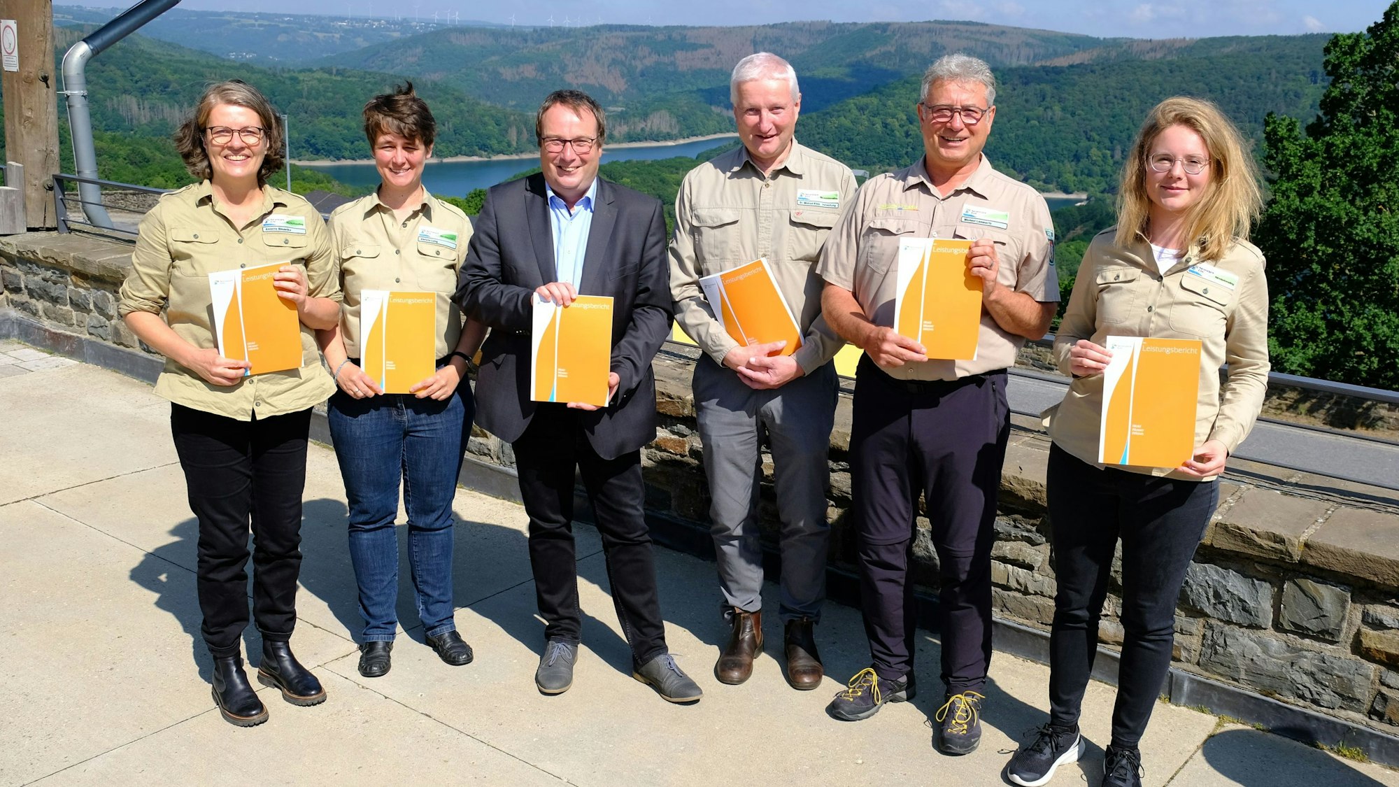 Mehrere Personen in Outdoorkleidung und ein Mann im Anzug präsentieren den Jahresbericht des Nationalparks Eifel.