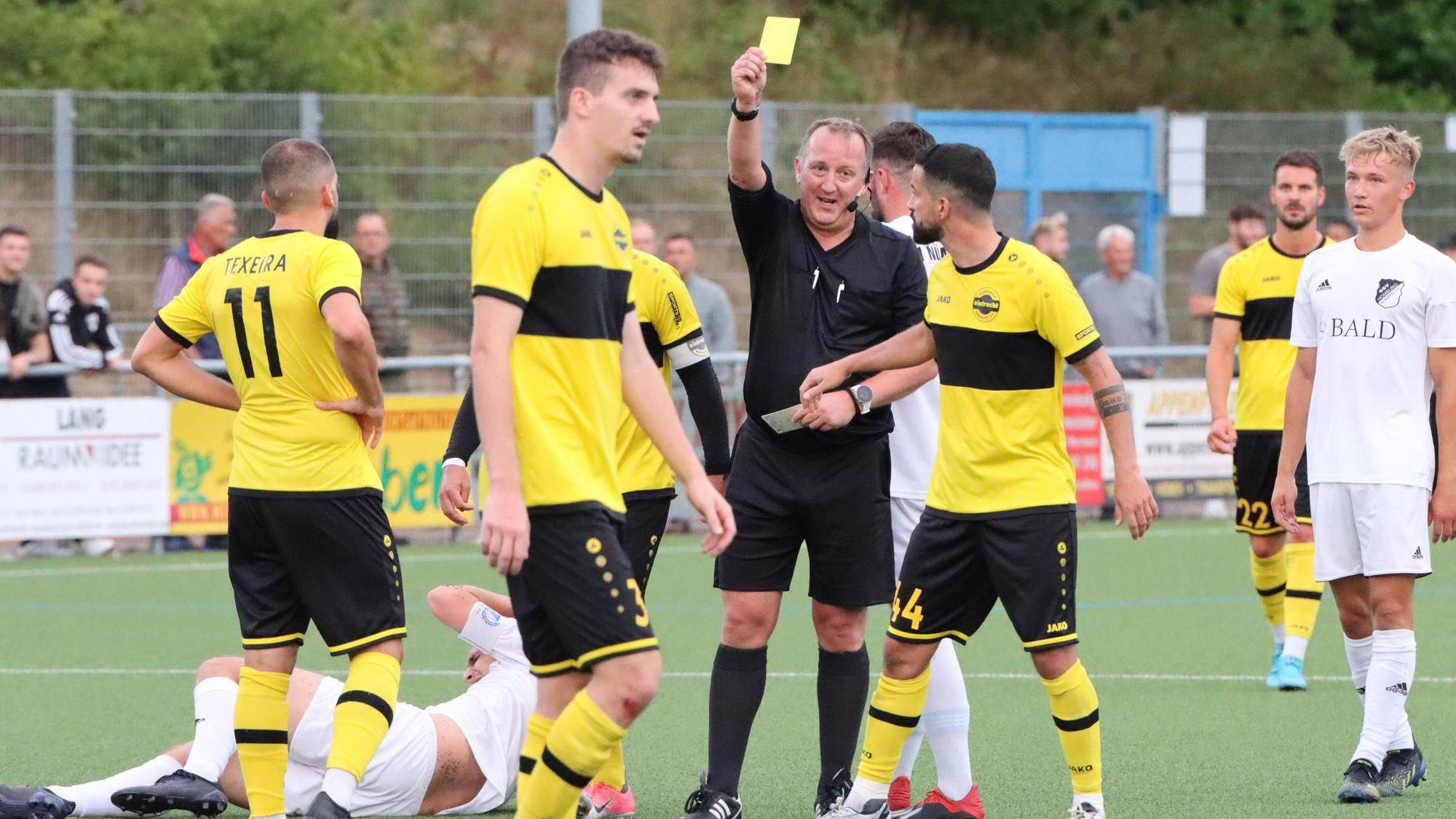 Ein Schiedsrichter zeigt einem Fußballspieler die Gelbe Karte.