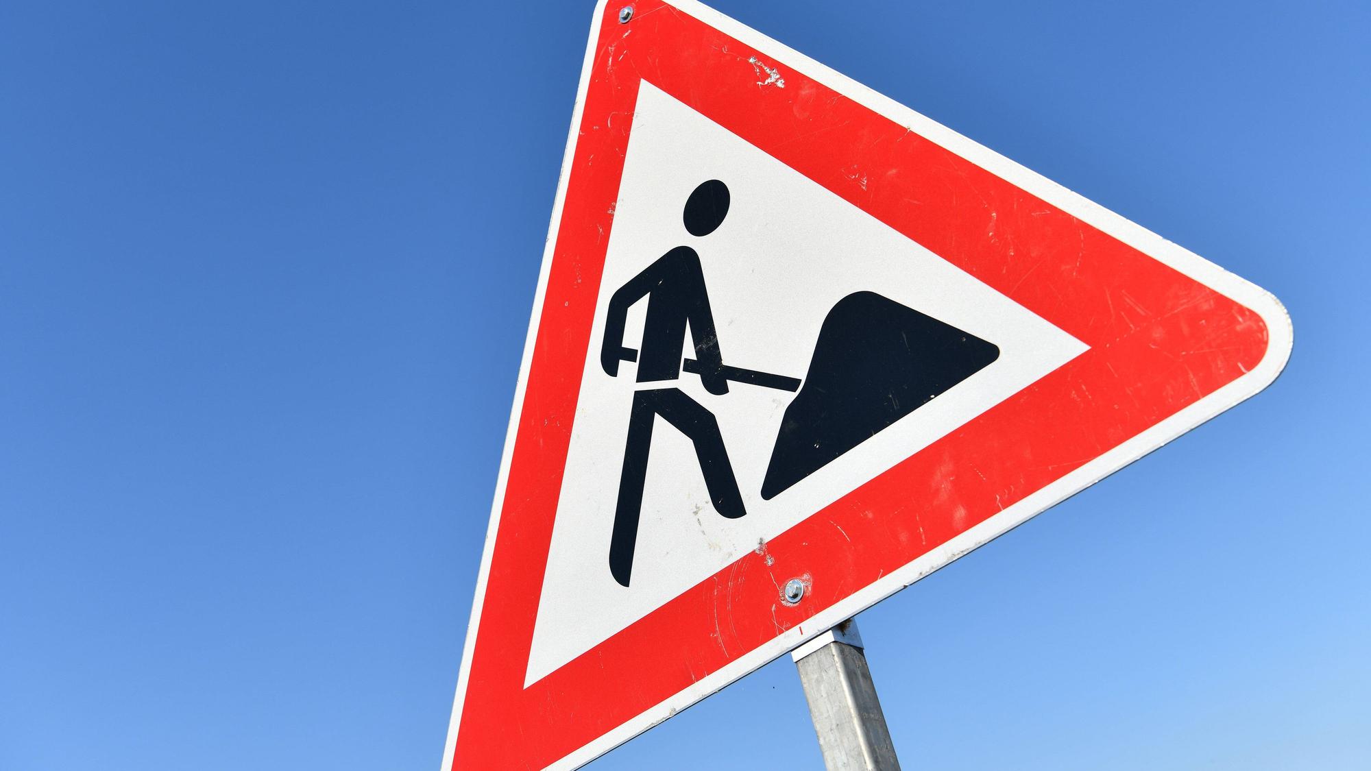 Zu sehen ist das Verkehrszeichen „Achtung Baustelle“ vor blauem Himmel.