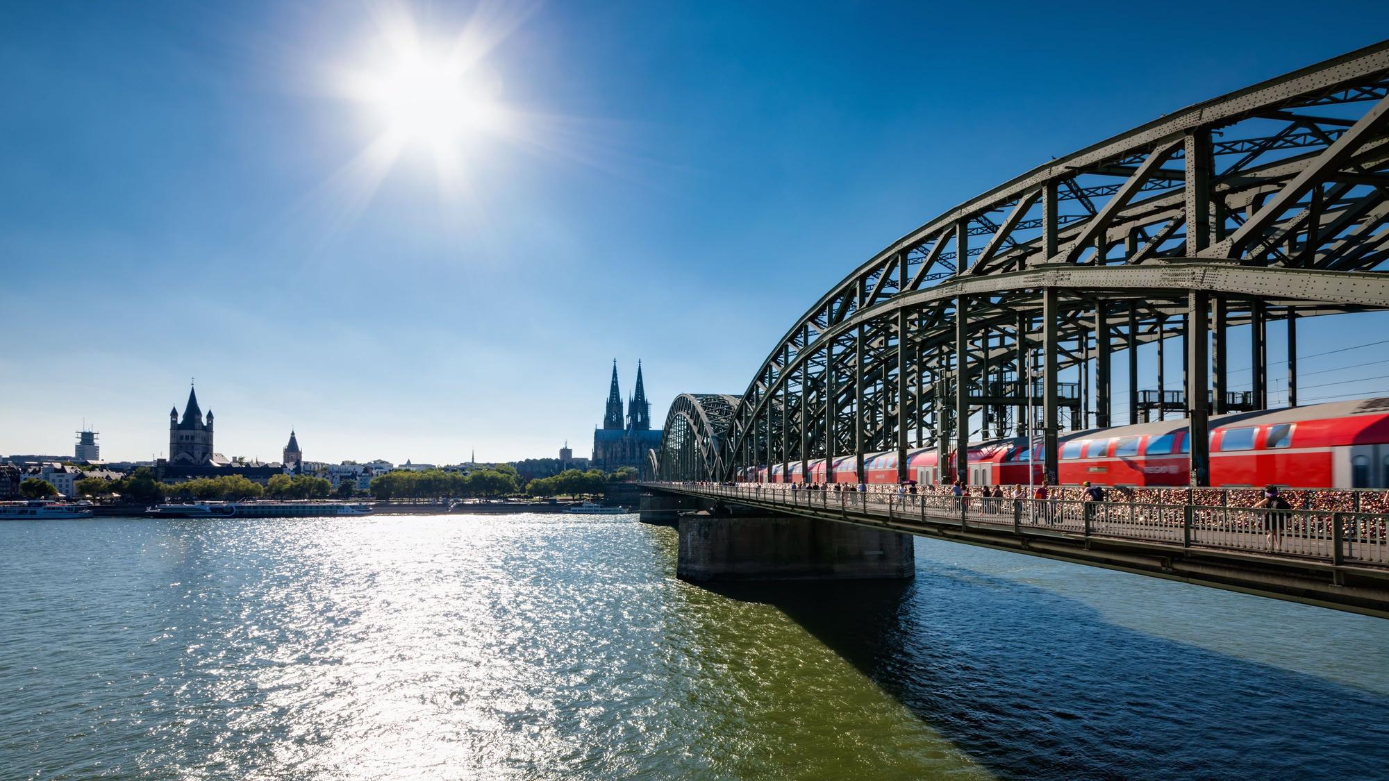 Blick auf die von der Sonne angestrahlte Hohenzollernbrücke über den Rhein, im Hintergrund der Kölner Dom