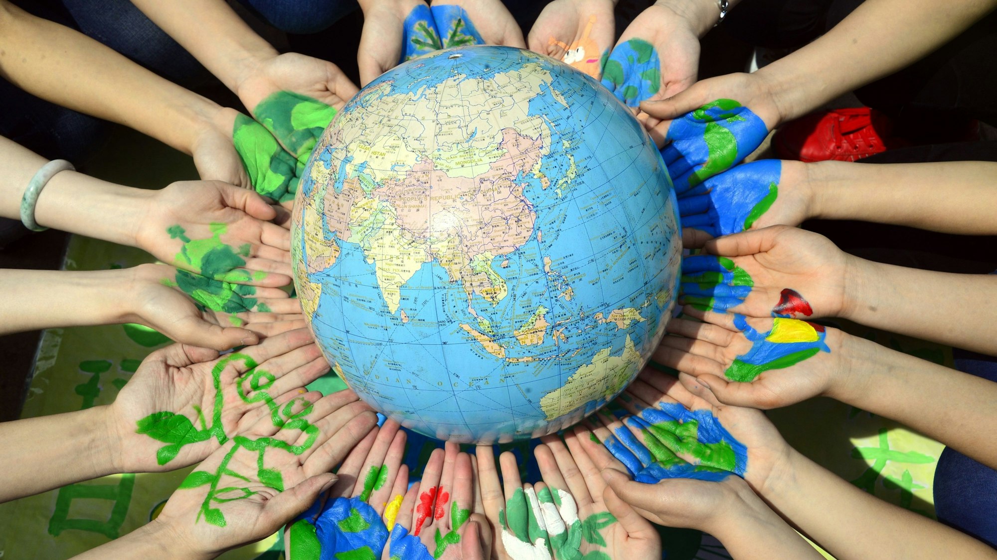 Studenten halten einen Globus in ihren bemalten Händen.