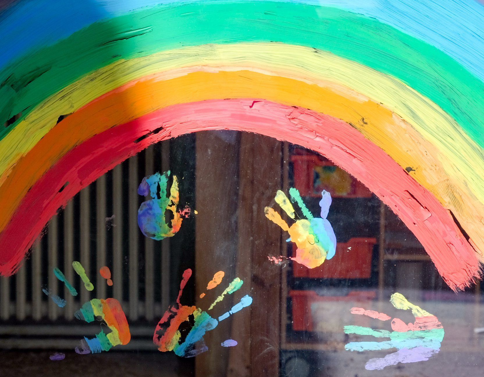 Kinderhände und ein Regenbogen sind an einer Kita zu sehen.