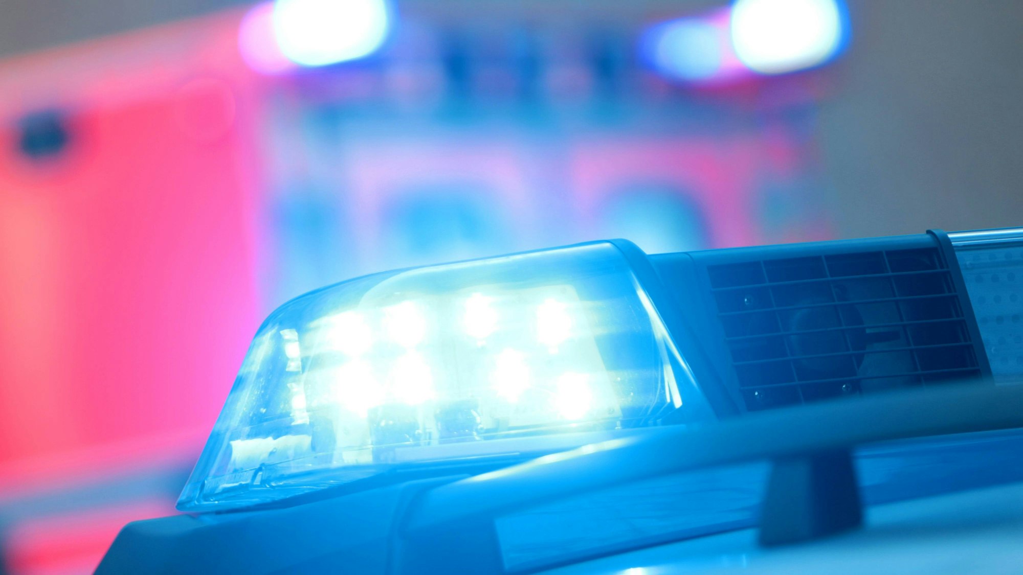 Ein Polizeiwagen mit eingeschaltetem Blaulicht und ein Rettungswagen bei einem Einsatz.